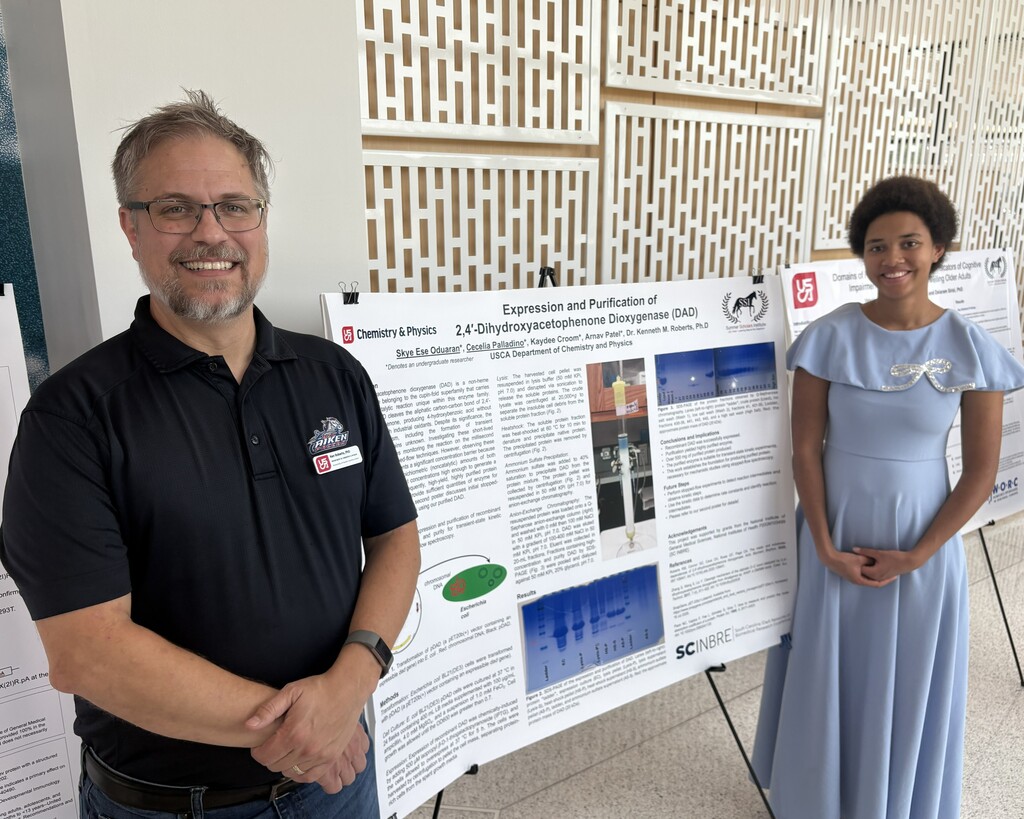 Student with professor presenting work on bulletin board. 