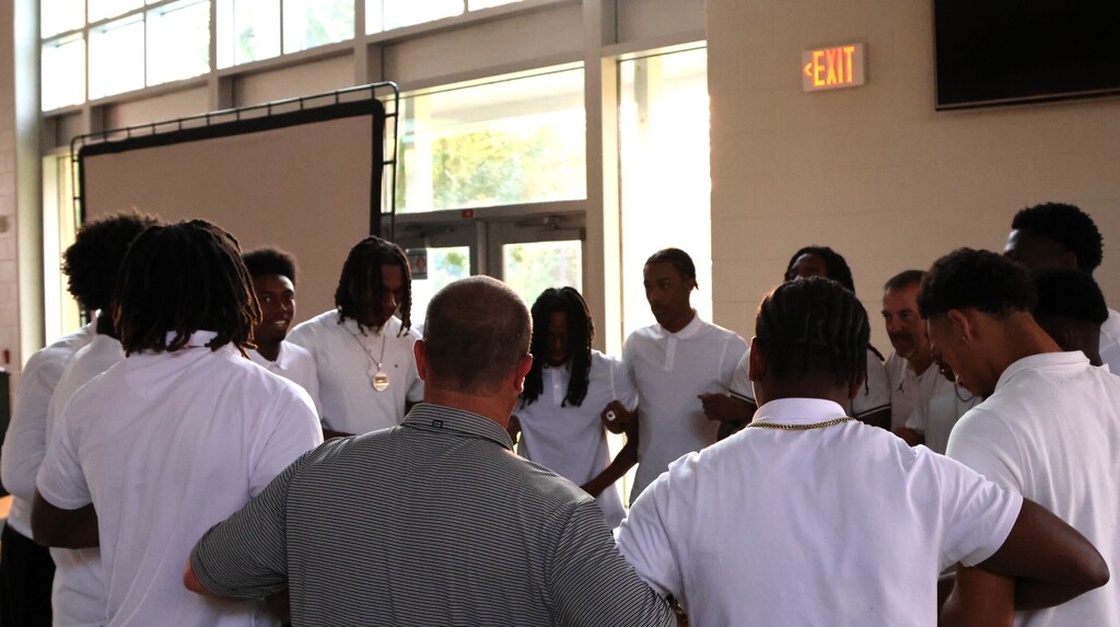 Coaches and players in a circle  arms linked in prayer. 
