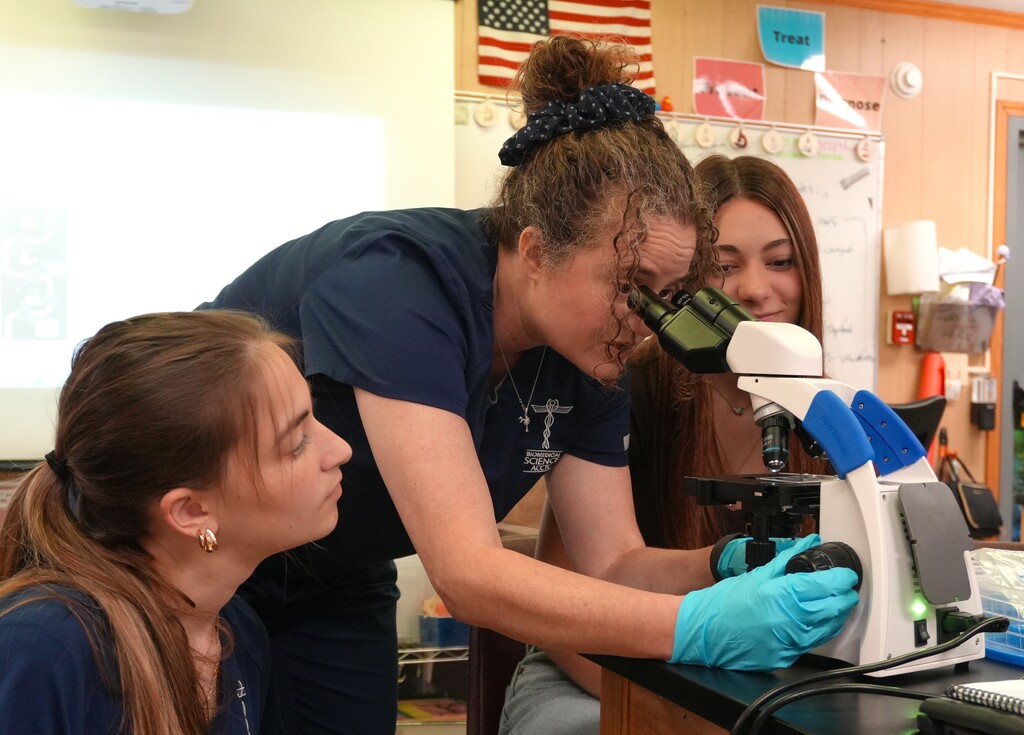 Dr. Palladino examines a specimen using a microscope while two students observe.