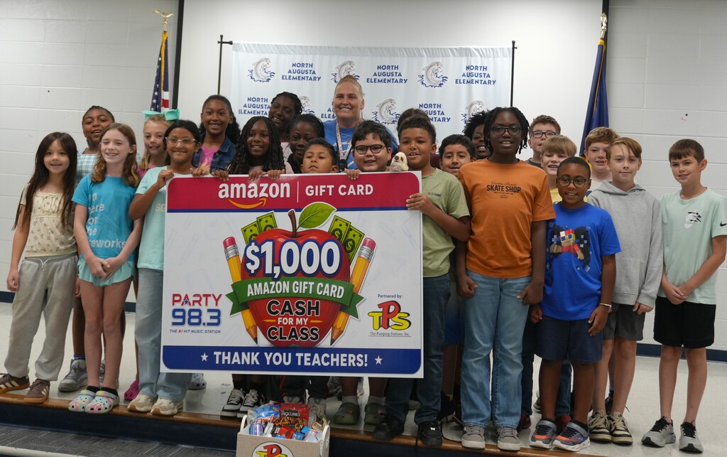 A group of children and an adult holding a large sign that says "Amazon Gift Card $1,000".