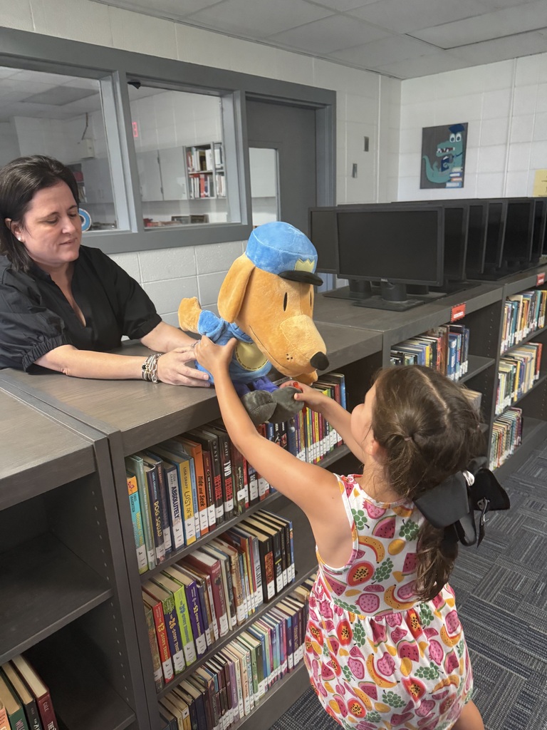 A woman and a young girl in a library, the girl is holding a toy dog while the woman sits behind a shelf.