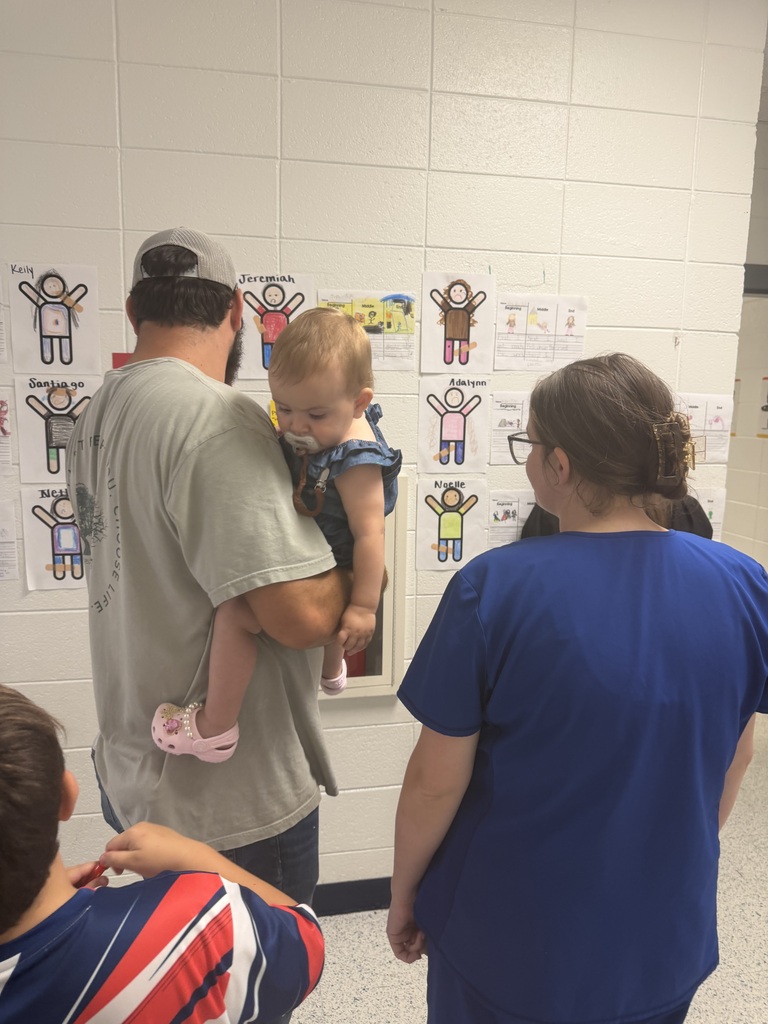 Man holds child; woman in blue looks at child. Wall with posters behind them.