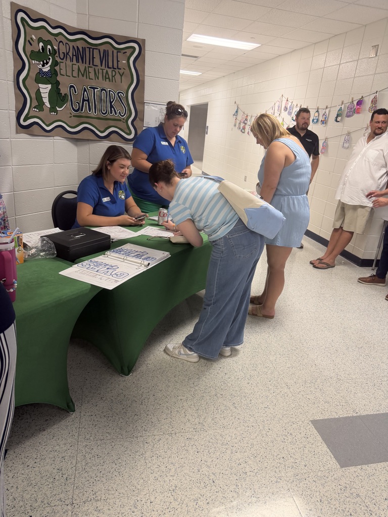 People gathered in a hallway with a green table. Two women sit at the table signing papers.