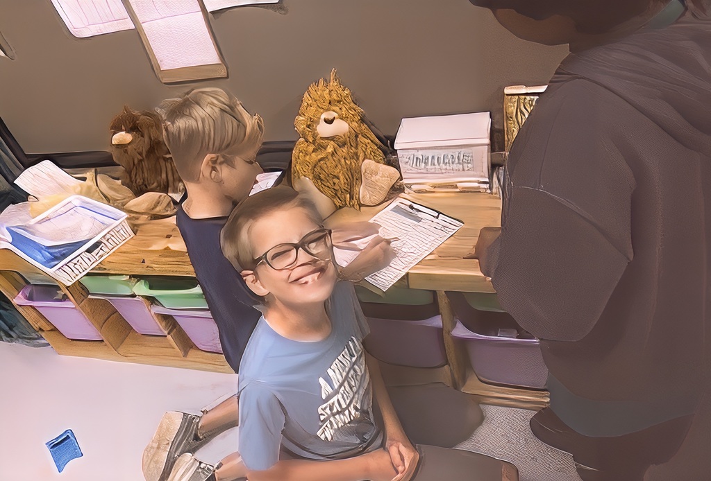 Two children sitting, one writing, a stuffed lion, and a box on a desk. Storage boxes and a wall with papers.