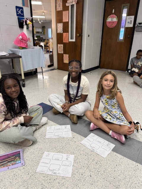Three children sit on the floor with worksheets, two wearing glasses. Behind them, a door leads to another room.