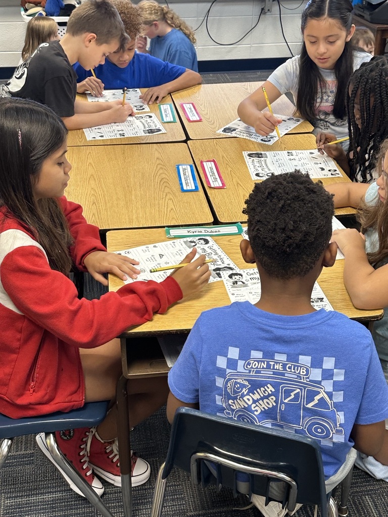 A classroom with children sitting at desks, working on worksheets, and interacting with each other.