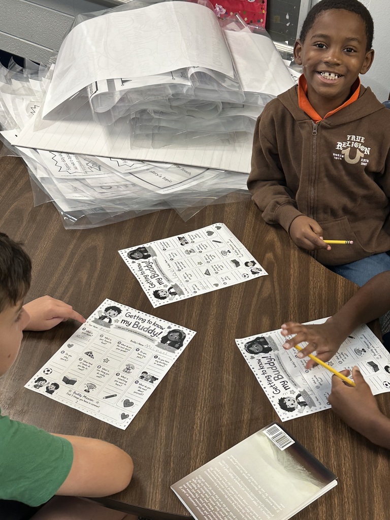 Students at a table with worksheets and pencils. A boy in brown and a boy in green.