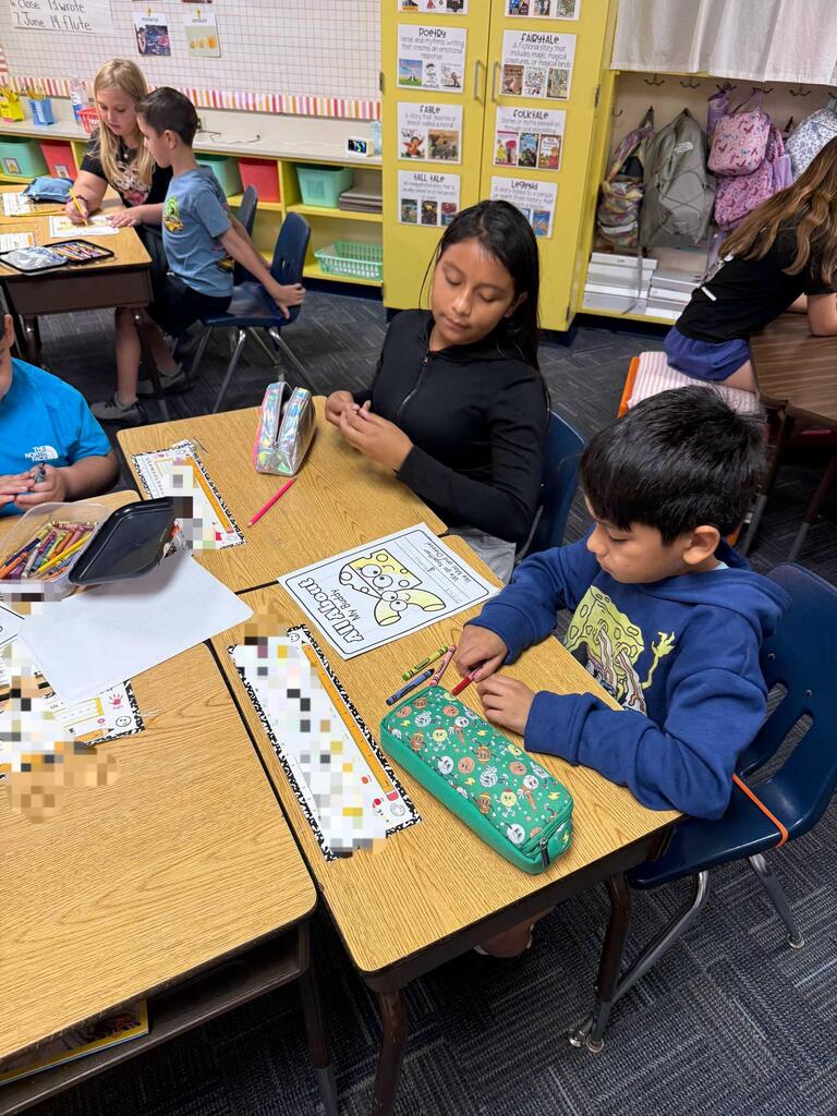 Children work on a craft project using tiles at desks in a classroom with yellow cabinets and a white curtain.