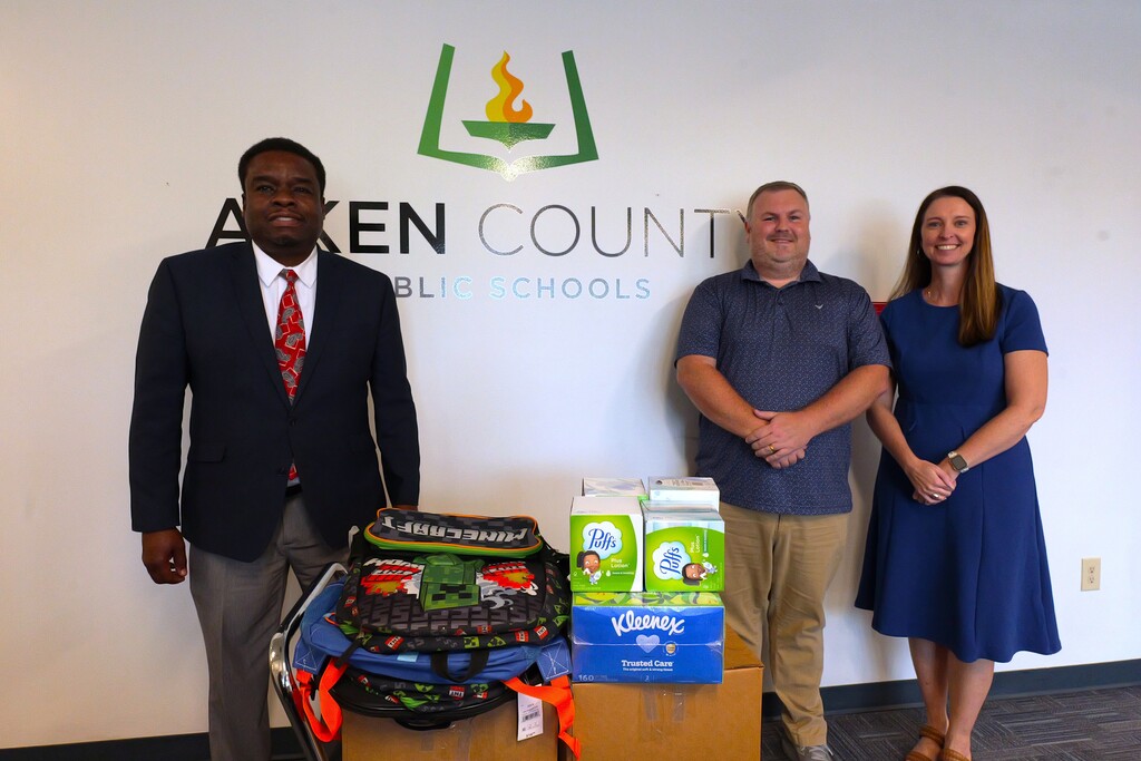 Two district employees, along with a Fort Gordon representative pose for a photo with donated items for students in the district.