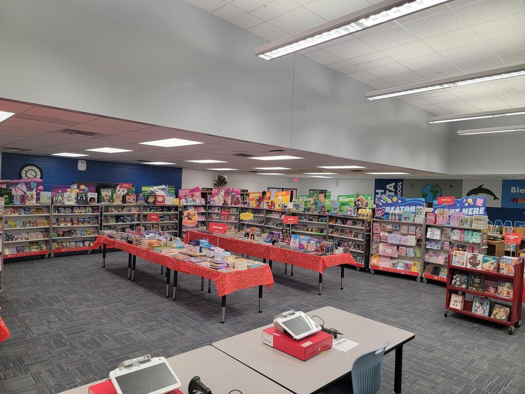 Library with tables, shelves, and books. Long tables covered in red fabric. Tables have monitors on them.