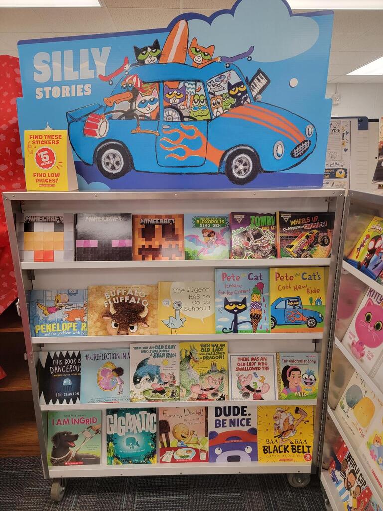 A bookshelf with colorful book covers displayed, topped with a "Silly Stories" sign featuring a blue car.