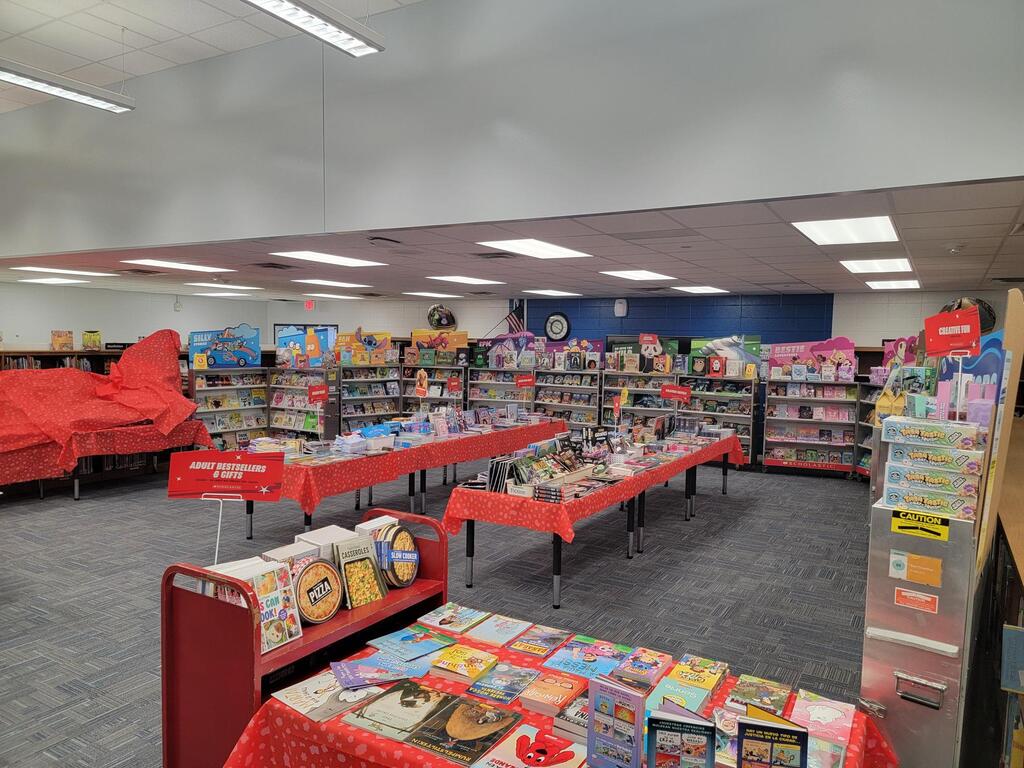 Interior of a book store with red tables and carpets. Books on tables and shelves, along with a blue wall and ceiling lights.
