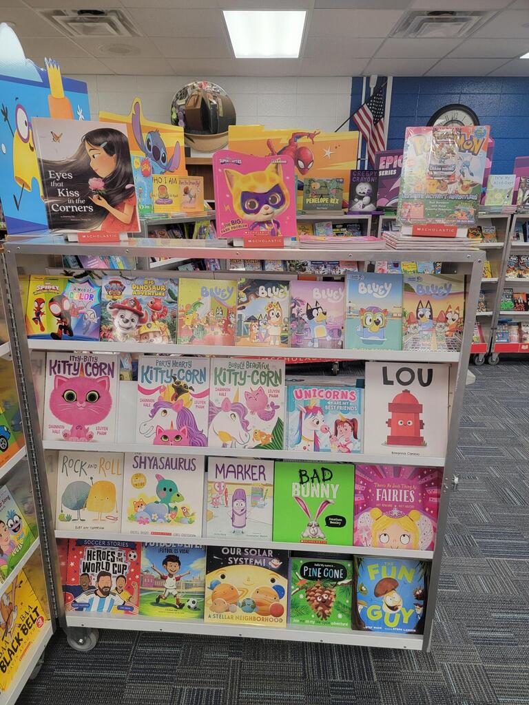 A book shelf displays various colorful children's books in a library setting, with some books featuring cartoon characters.