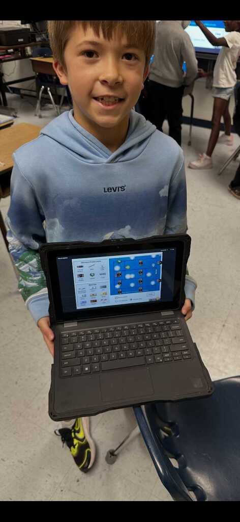 A child holding a laptop with a colorful screen displaying icons. He wears a blue hoodie with "LEVIS" on the back.