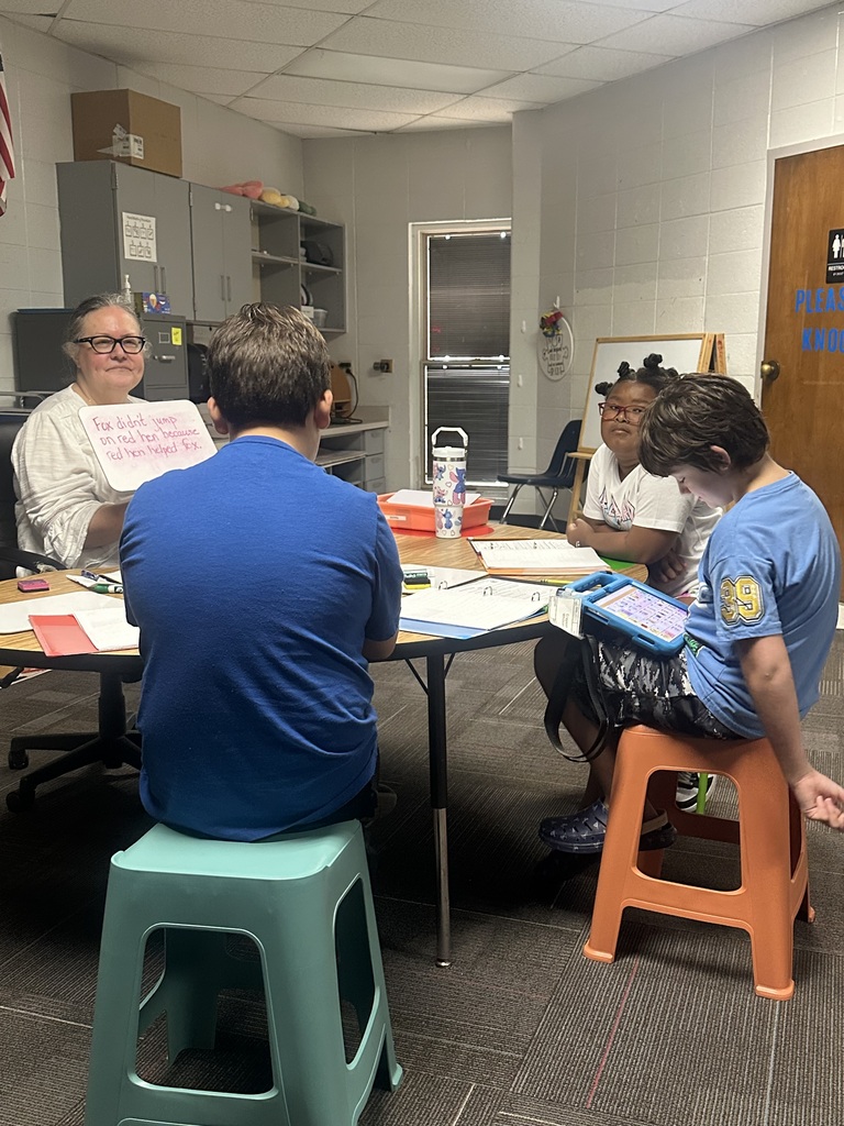 Four people sit around a table; one adult and three children. A woman holds a pink paper.