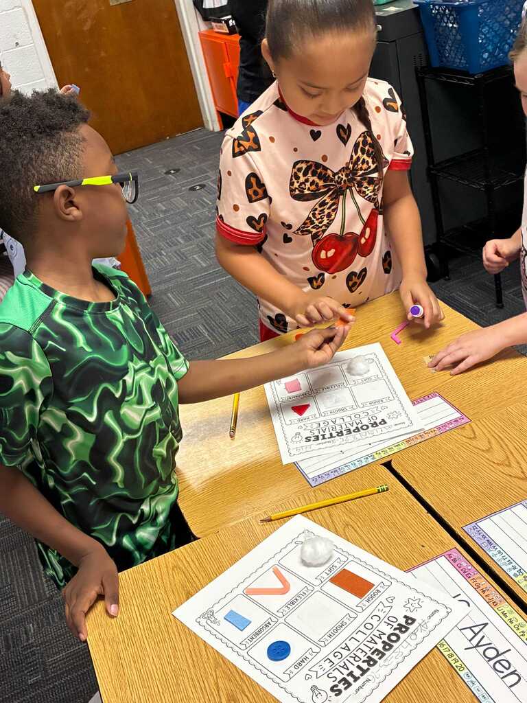 Children sitting at a desk, working on a worksheet with shapes, colors, and names.