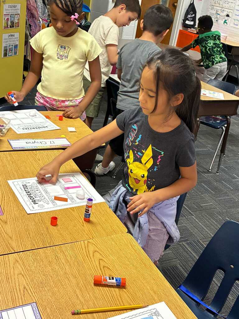 Children in a classroom seated at desks, engaged in an activity with paper and art supplies.