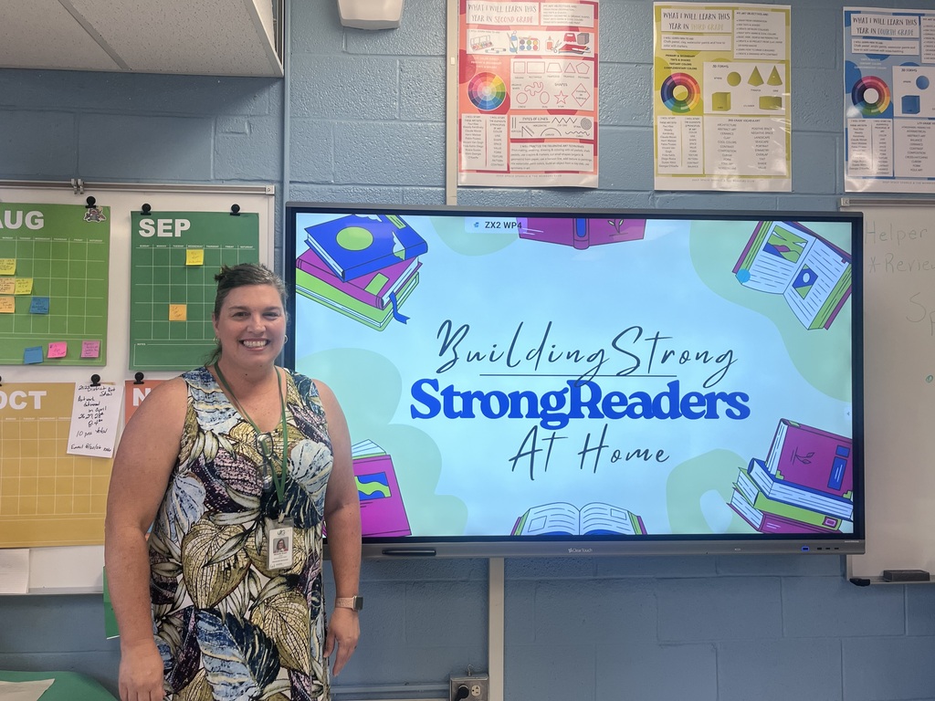 A woman stands in front of a classroom screen displaying the text "Building Strong Strong Readers At Home".