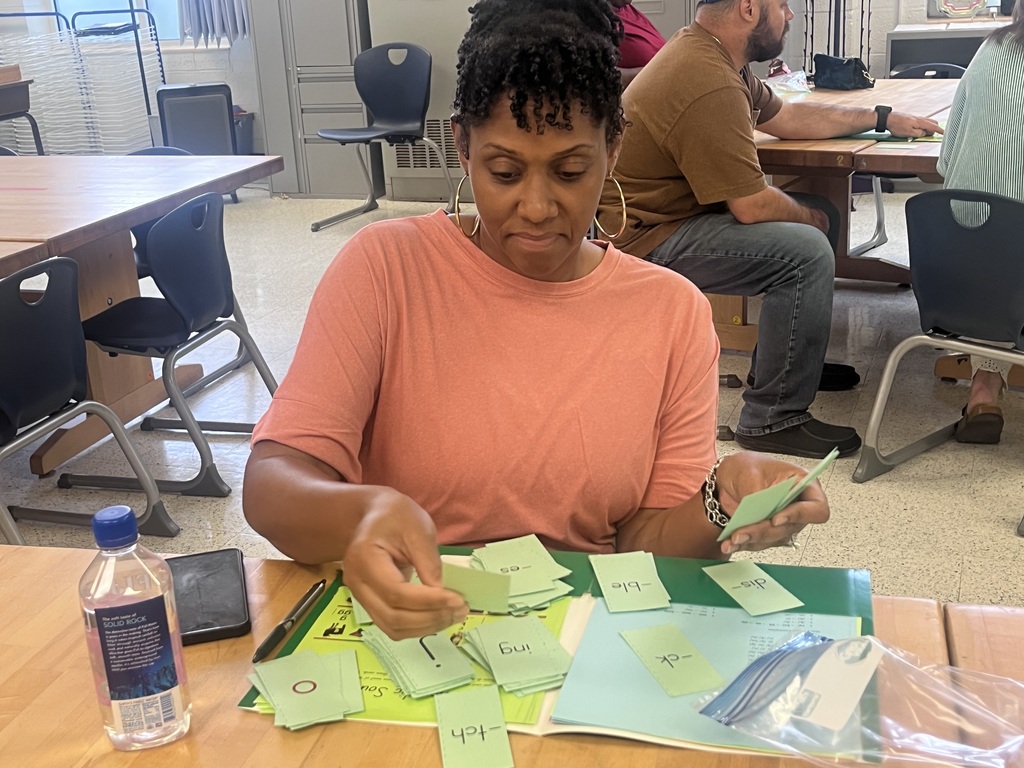 A woman in a peach shirt is seated at a desk, working on a project with paper and sticky notes.