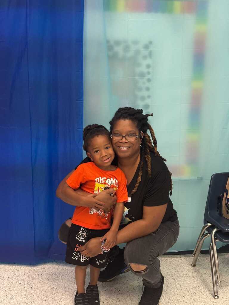 Woman wearing glasses and a black t-shirt holds a young boy with a bright orange t-shirt.
