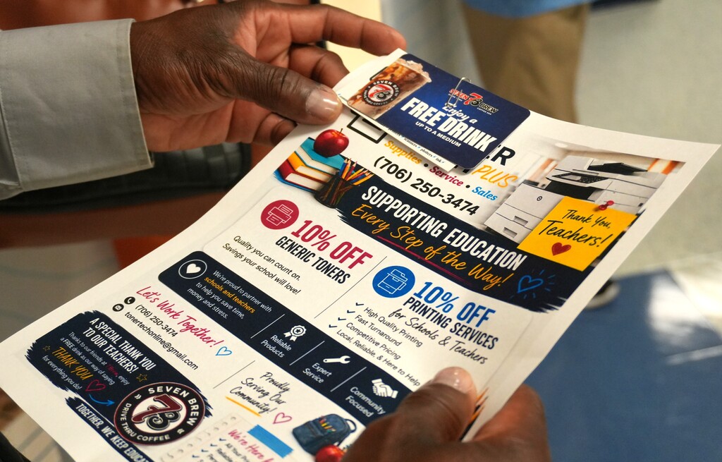 A hand holds a flyer with text about discounts, "Free drink," "10% off generic inks," "Supporting Education," and a logo.