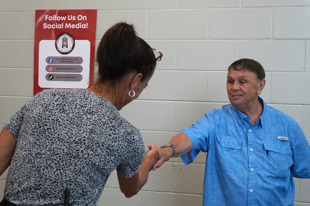 Two people shake hands. A woman in a floral shirt and a man in a blue shirt.