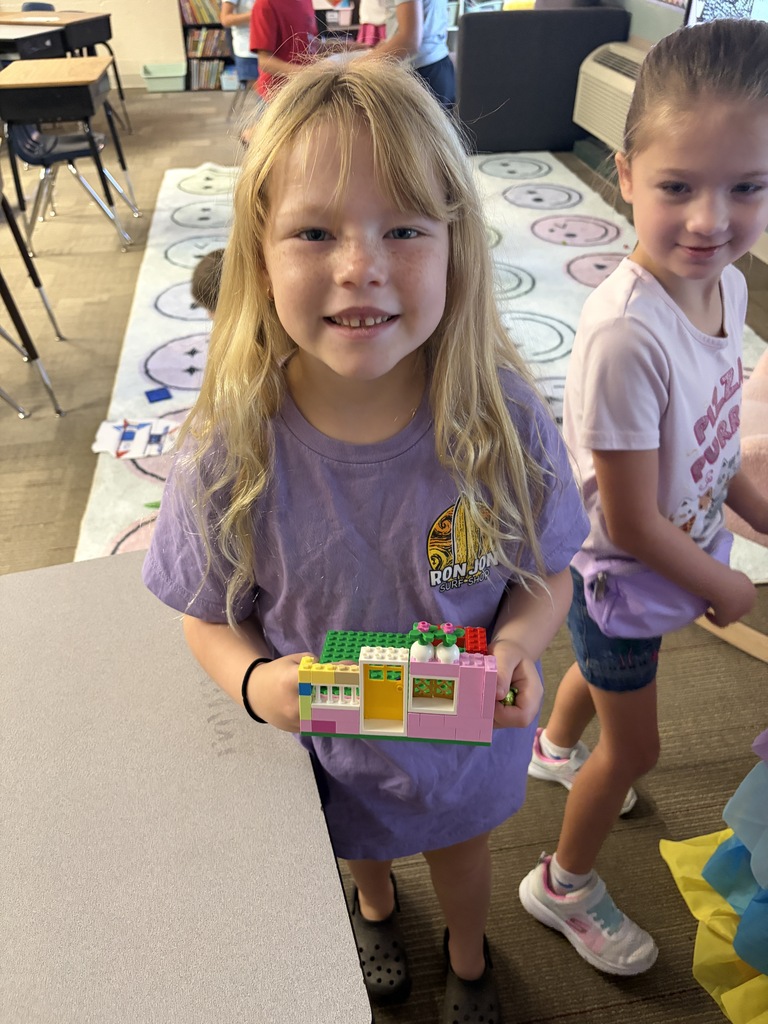 Two girls, one showing what they built with Lego blocks.