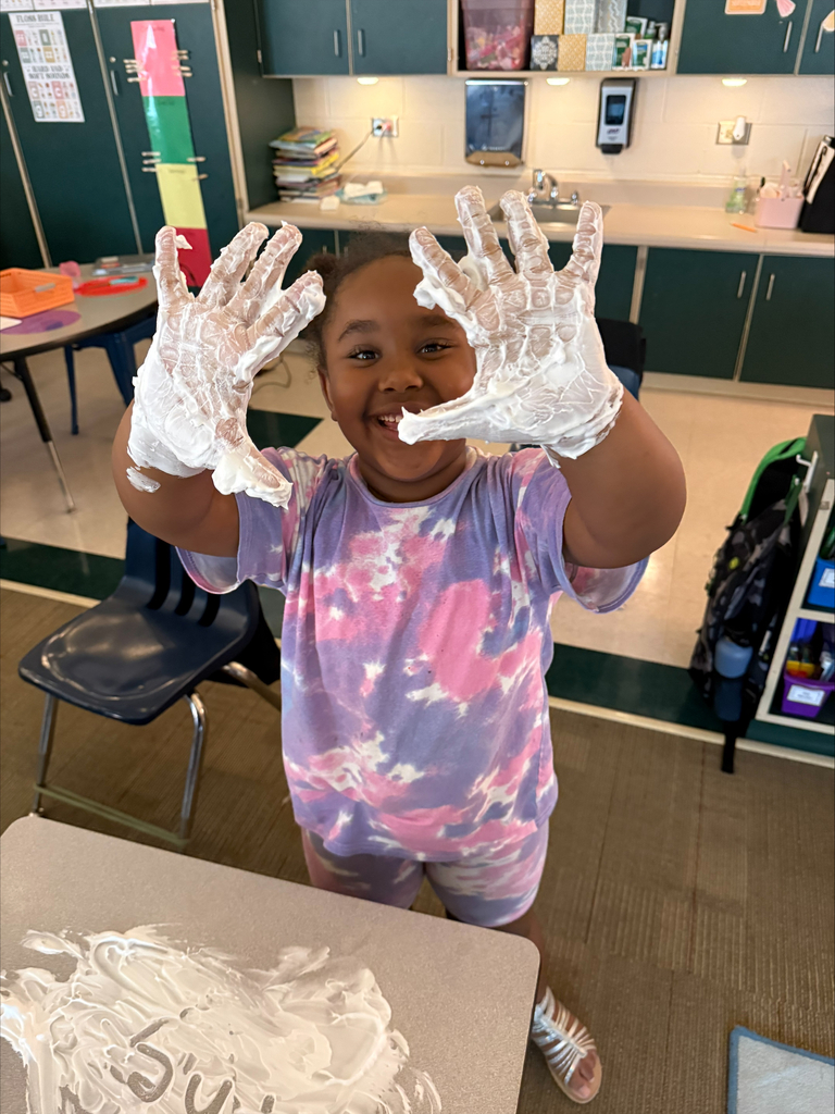 A girl holds up her hands covered in shaving cream.