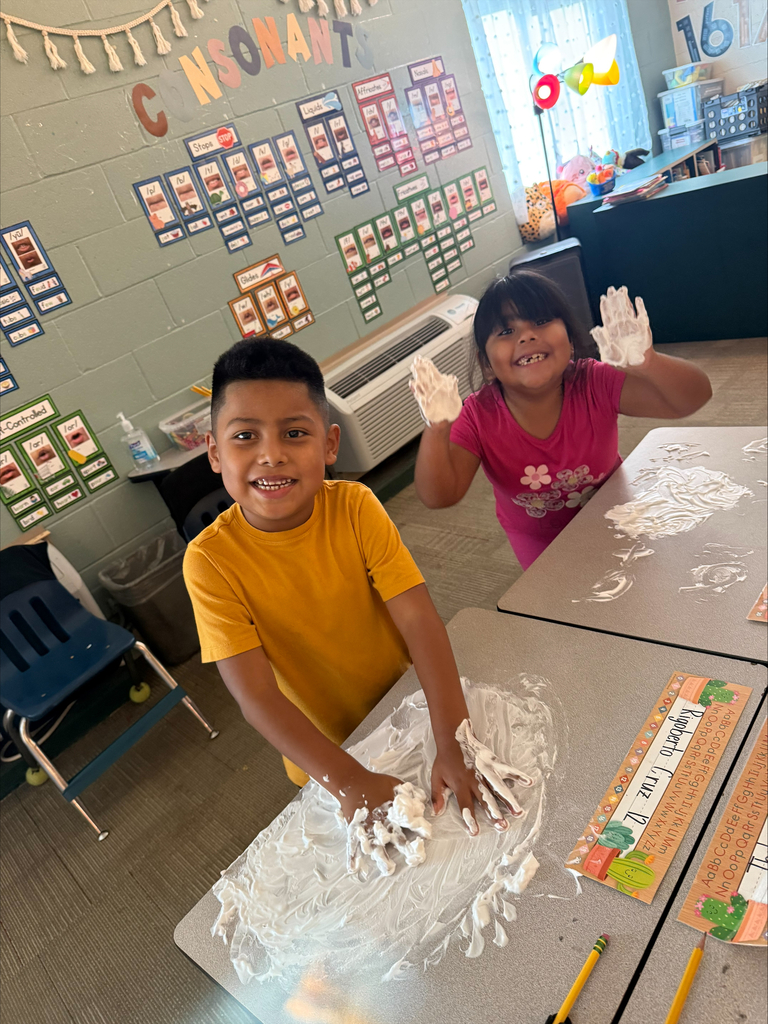 A boy and girl are writing with shaving cream on their desks.