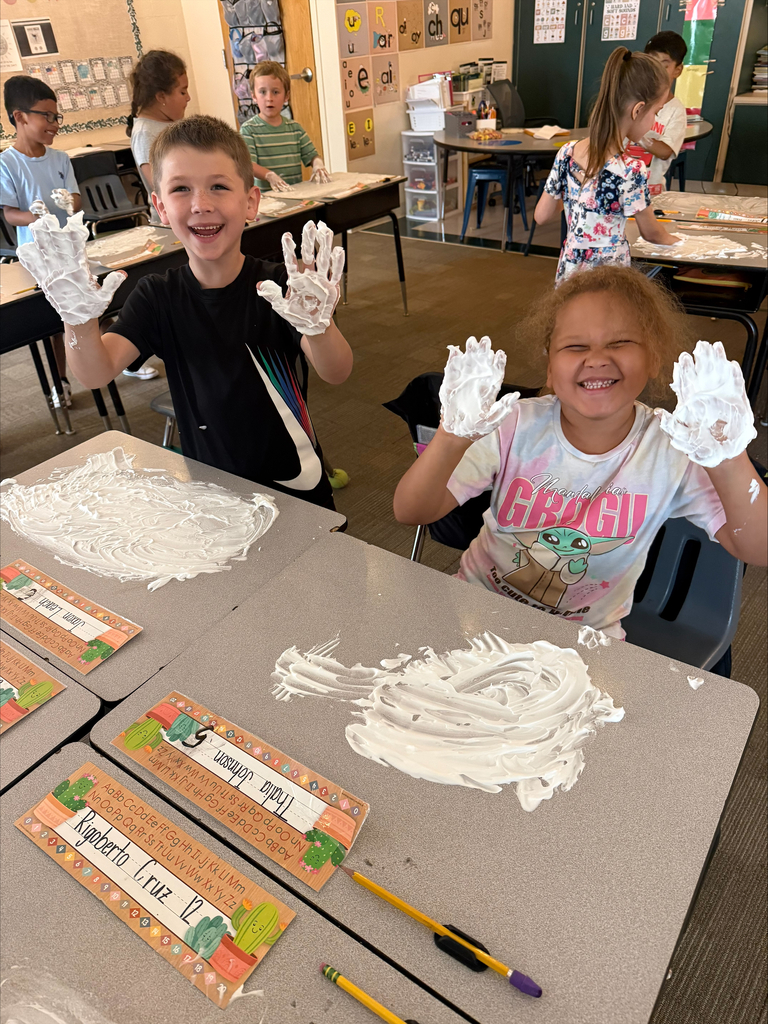 A boy and girl smile while showing their hands covered with shaving cream.