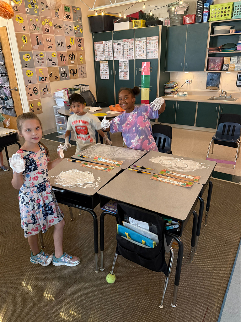 Three students stand by their desks with shaving cream covering their desks and hands.