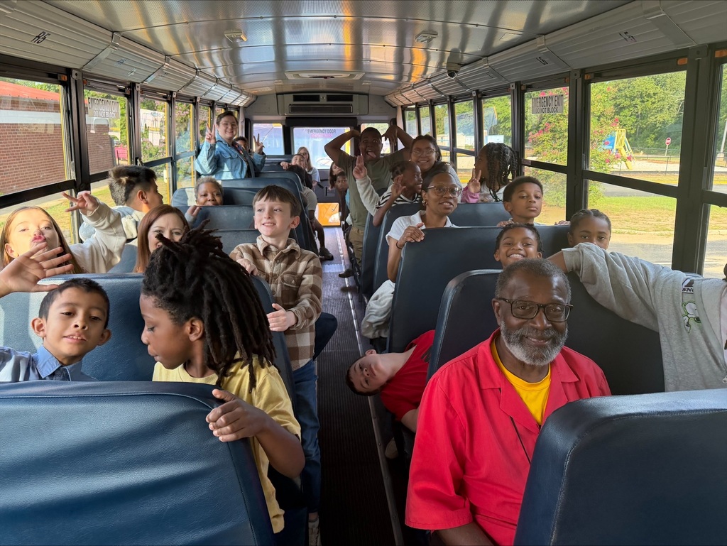 A group of children and adults inside a school bus. Some sit and others stand, with one man wearing a red shirt.