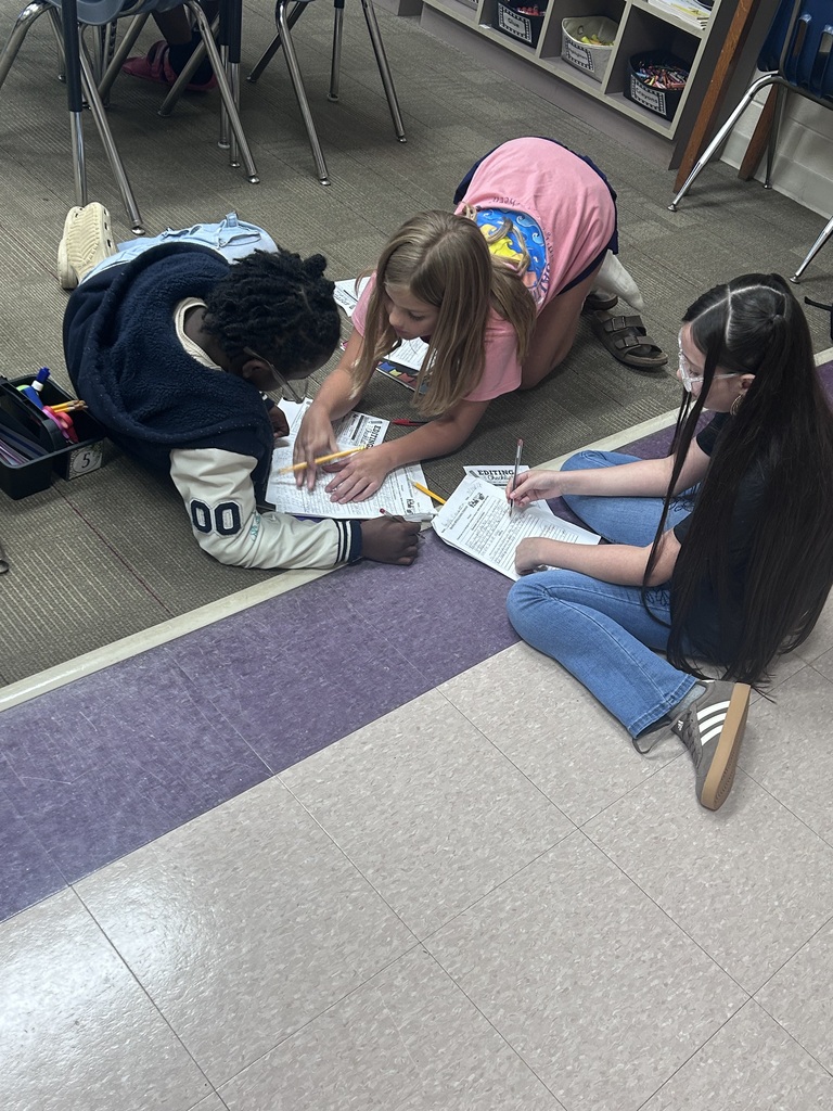 Three students sit on the floor discussing their writing.