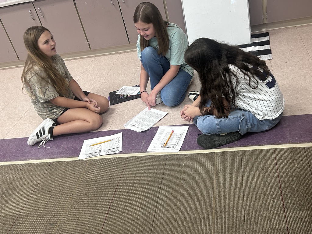 Three girls sitting on the floor discuss their writing.