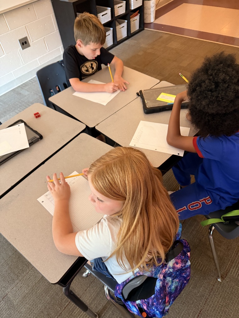 Three students are writing at their desks.