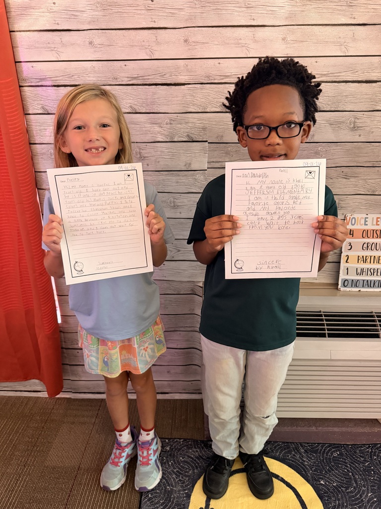 A boy and girl hold up their completed writing papers.