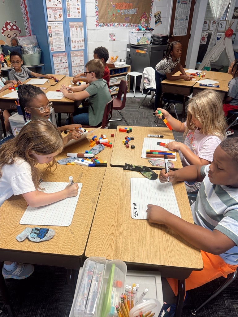 Children wearing glasses seated at desks. They use crayons to color in their workbooks.