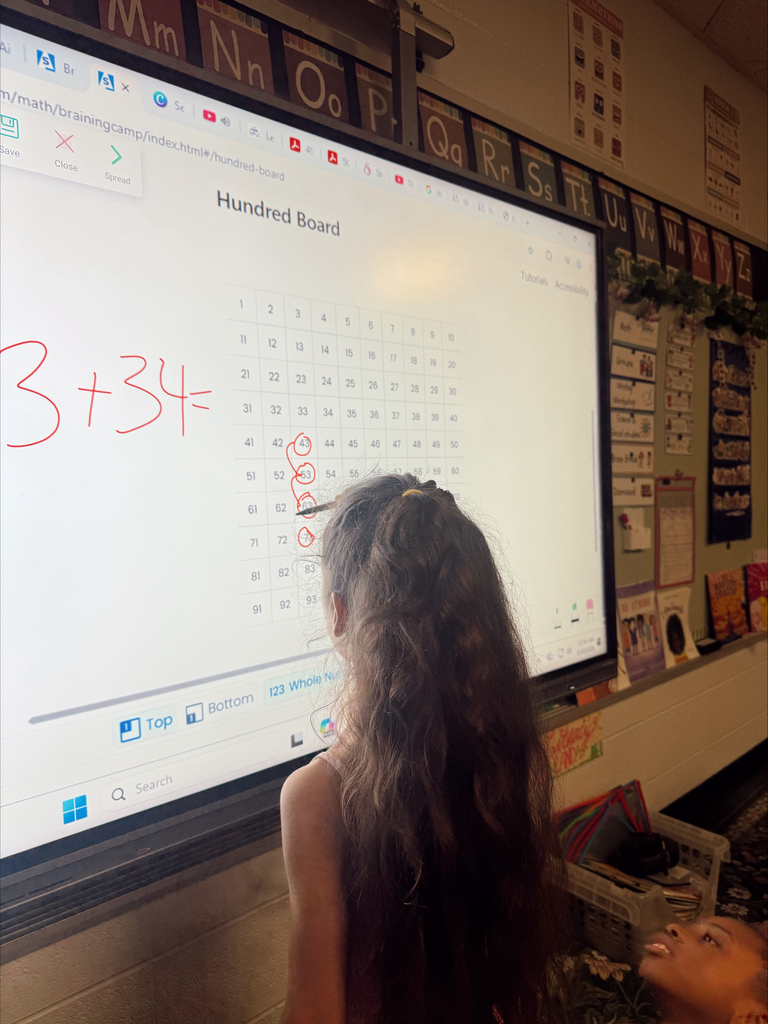 A girl watches a math problem on a classroom smartboard. The board displays the equation 3+34=.