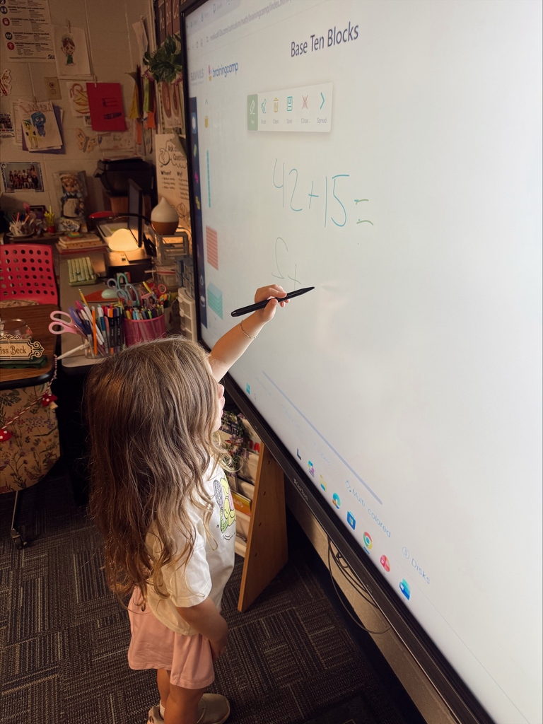 A young child writing on a whiteboard, using a marker to draw a number. The whiteboard is mounted on a wall.