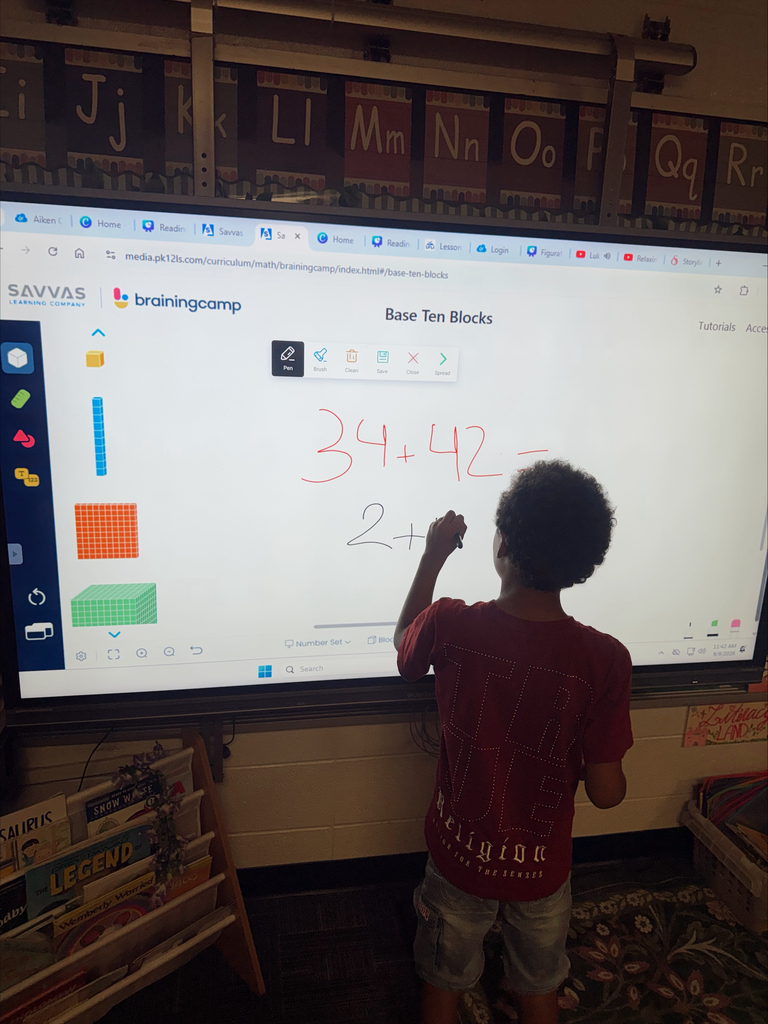 Child stands at a large screen, writing on an interactive whiteboard with a math equation.