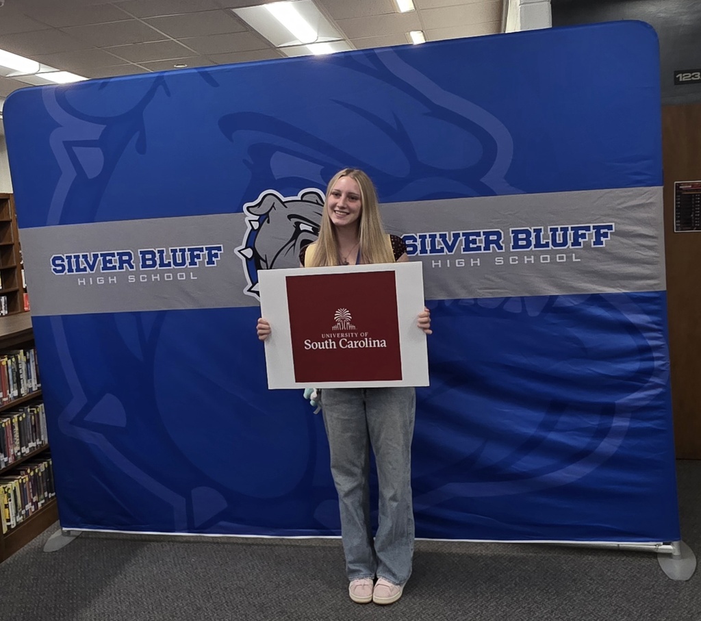 Female student in front of Silver Bluff High School blue backdrop holding a college sign