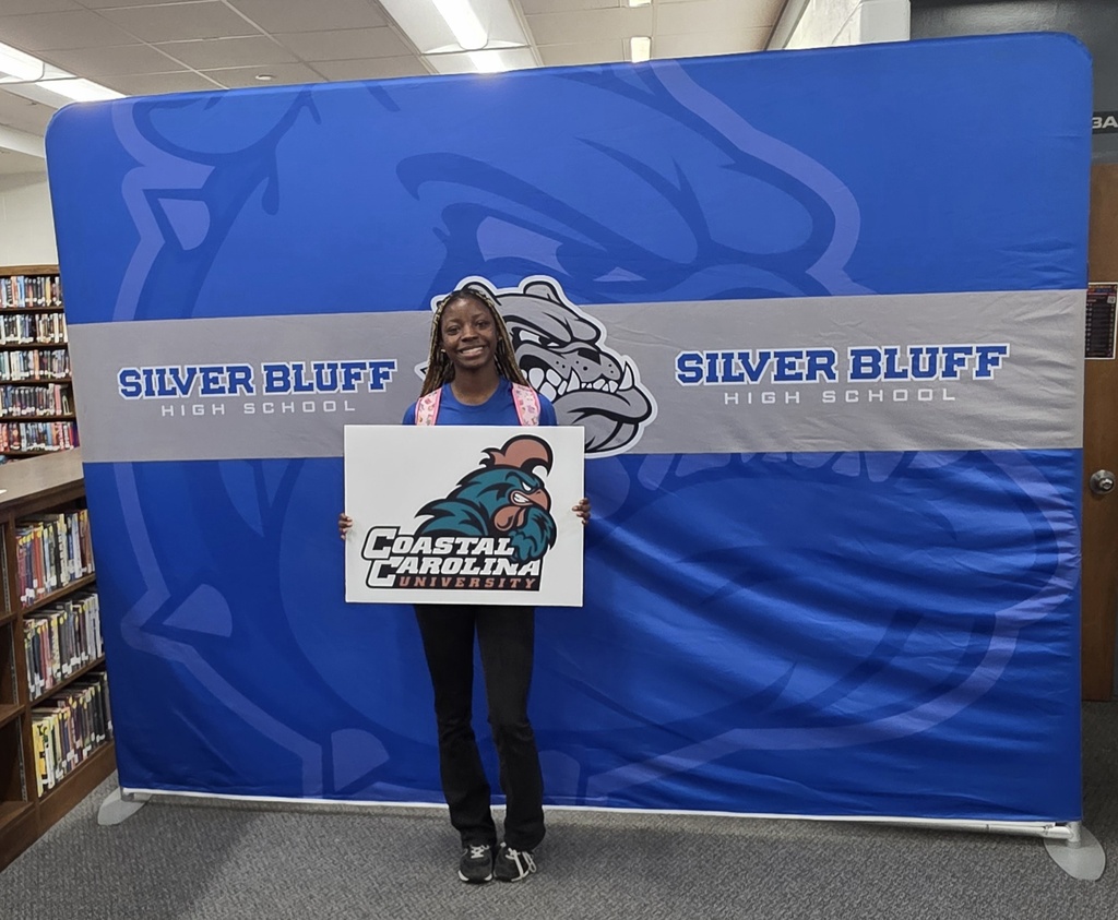 Female student in front of Silver Bluff High School blue backdrop holding a college sign