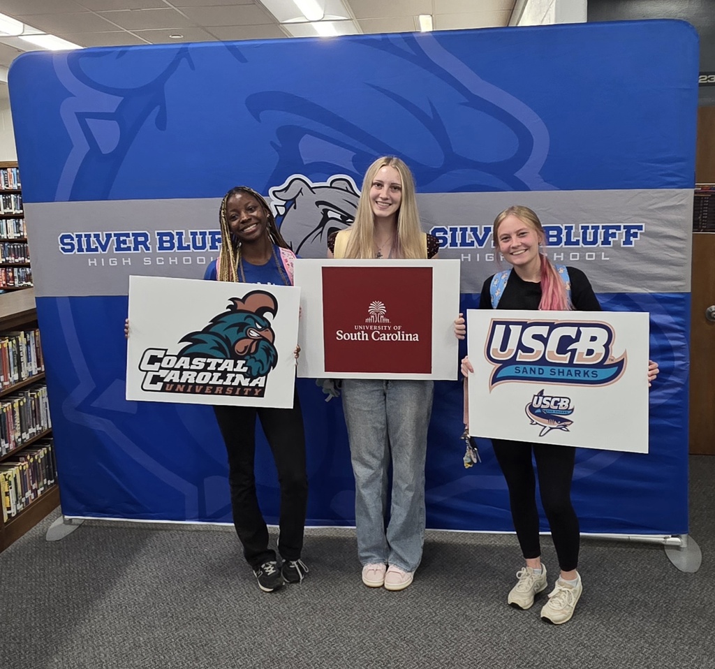 Female students in front of Silver Bluff High School blue backdrop holding a college signs