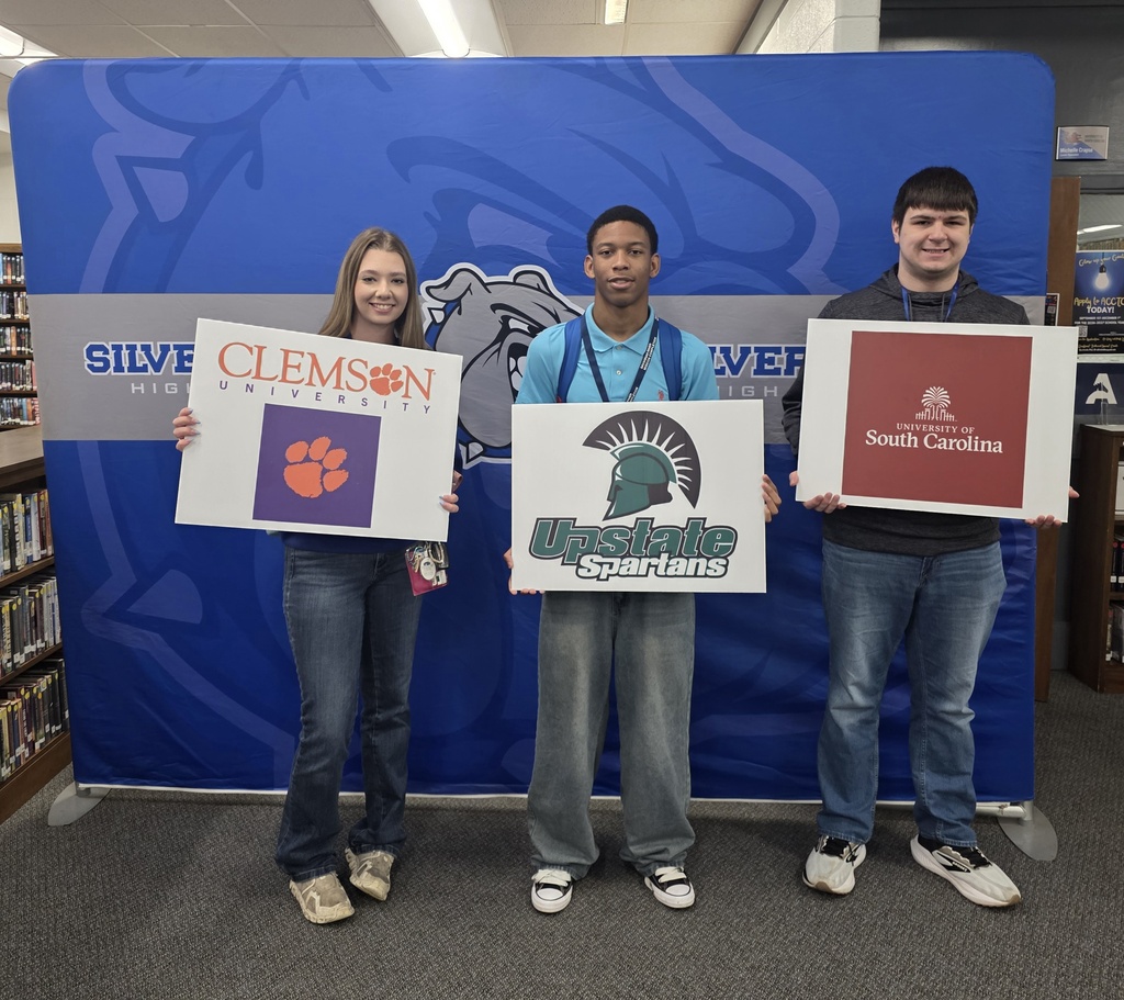 Students in front of Silver Bluff High School blue backdrop holding a college signs