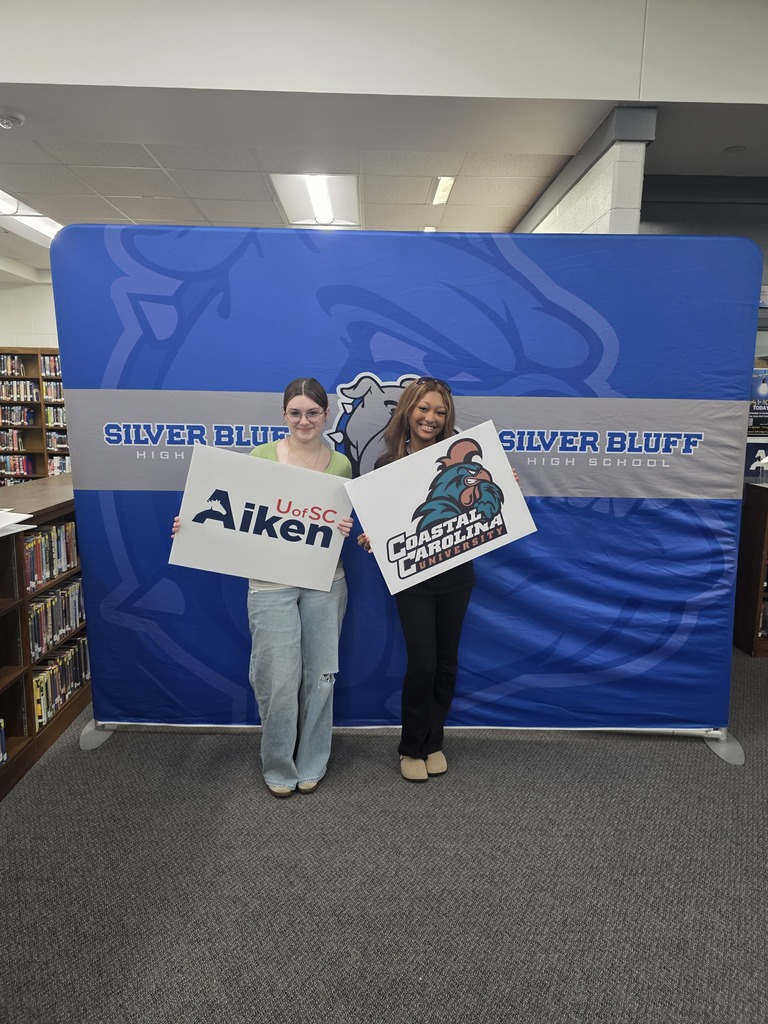 Students in front of Silver Bluff High School blue backdrop holding a college signs