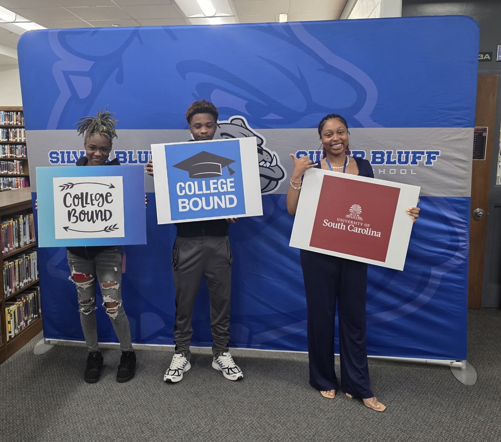 Students in front of Silver Bluff High School blue backdrop holding a college signs