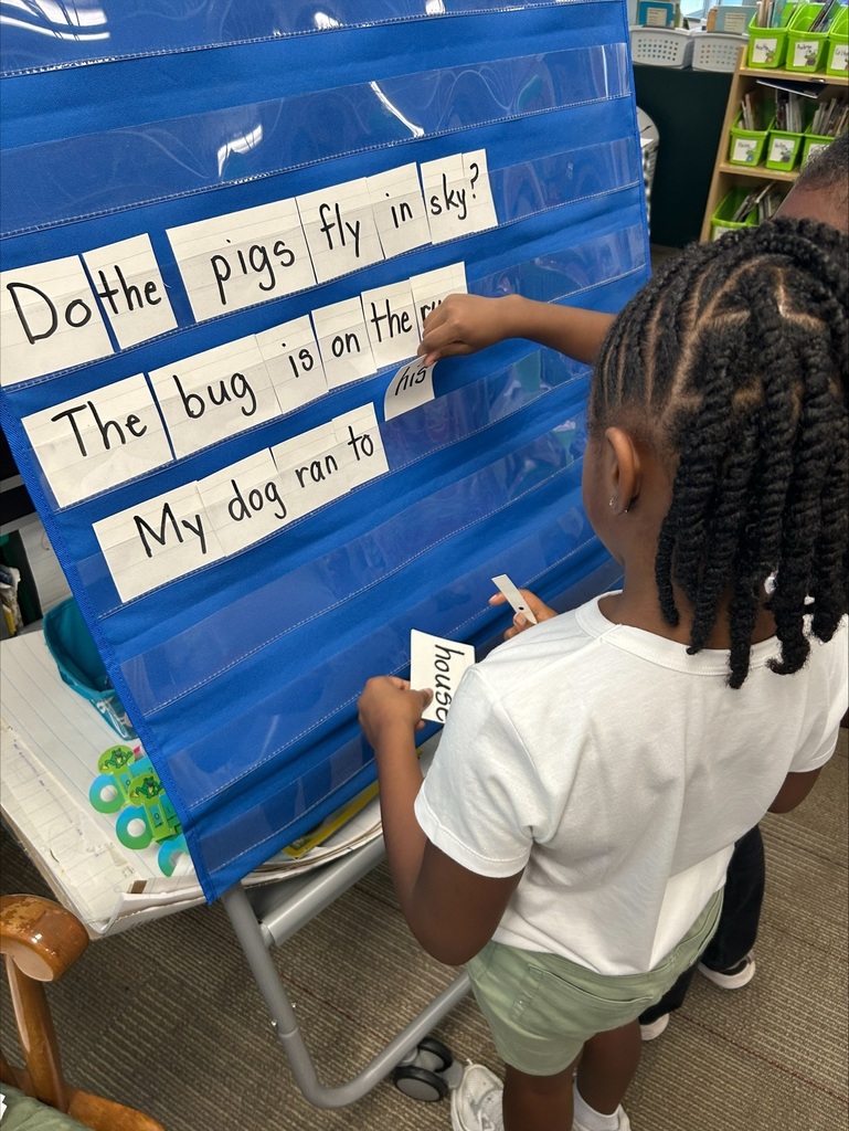 Two students are placing word flash cards into a pocket chart in sentence order.