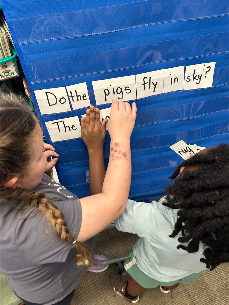Two students are placing word flash cards into a pocket chart in sentence order.