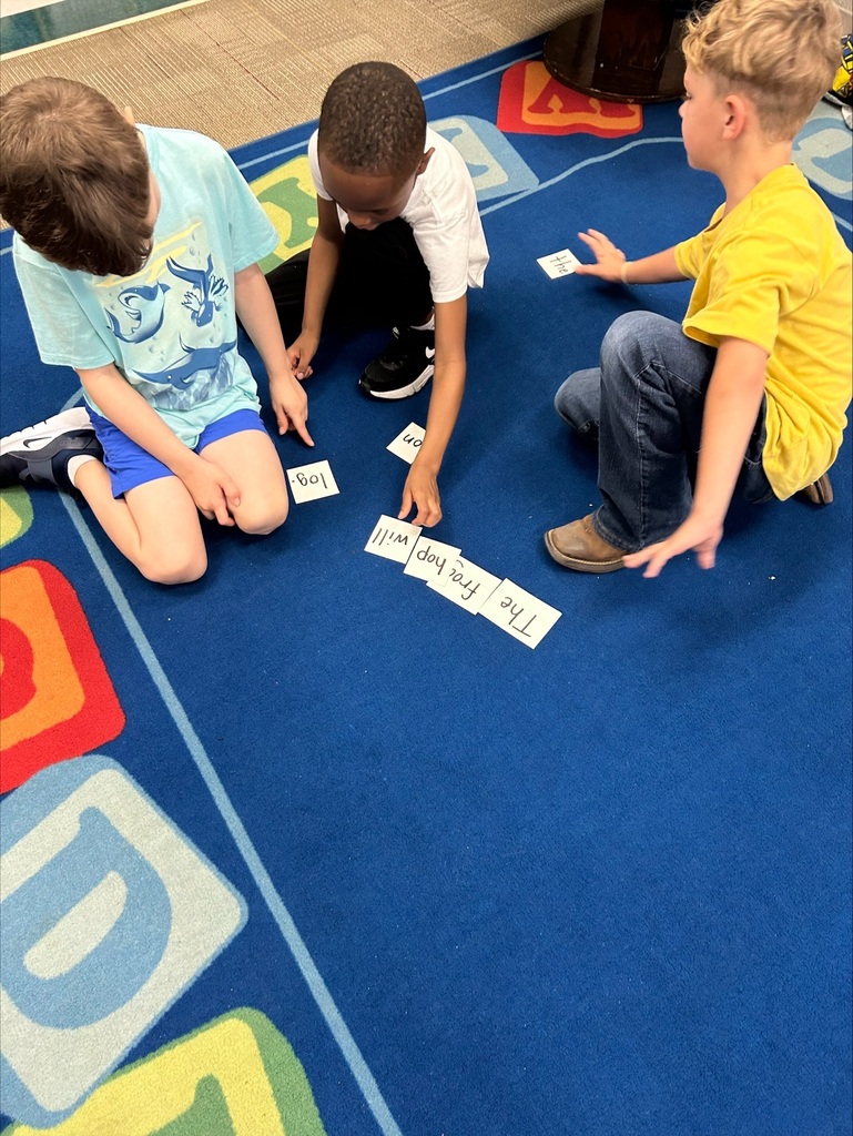 Three students are placing word flash cards into sentence order.