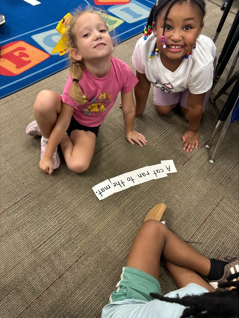 Two girls are smiling next to the sentence they created with word flashcards.